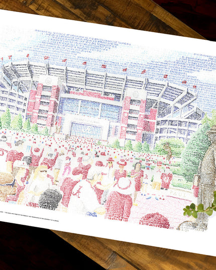 Unframed word art print of Bryant Denny Stadium in Alabama lies flat on wood table next to plant.