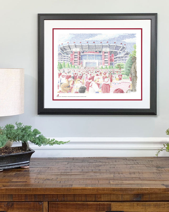 Matted and framed word art print of Bryant Denny Stadium in Alabama hangs on wall above wooden table.