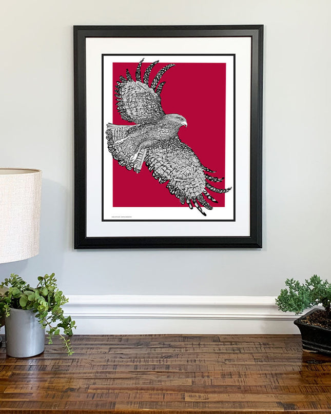 Framed art of St. Joseph Hawk with handwritten phrase "The Hawk Will Never Die" and red background on wall above dresser.
